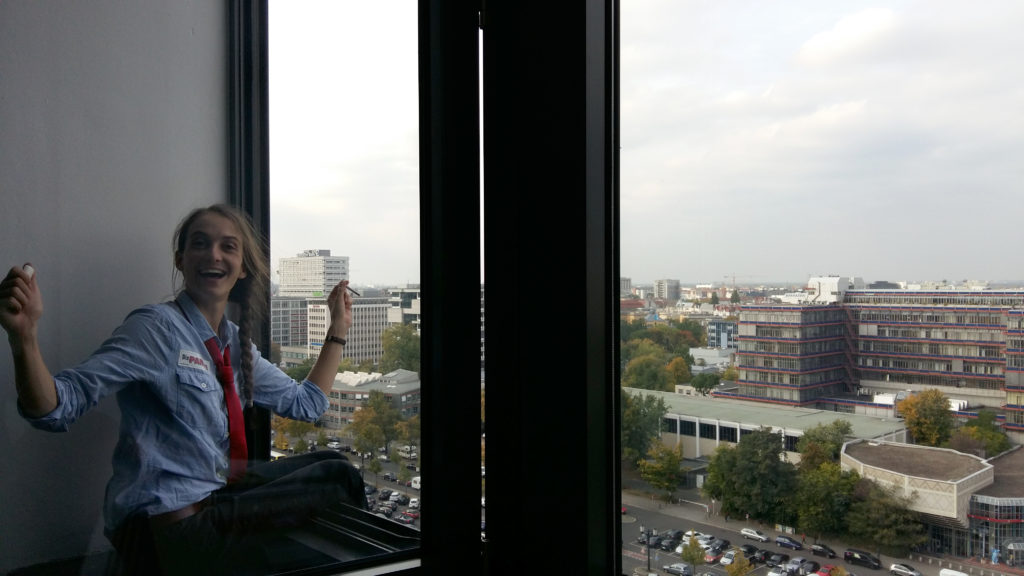 Eine Frau von der Partei „Die PARTEI“ raucht im Rahmen sitzend aus einem Fenster im 9. Stock des TU-Hauptgebäudes.